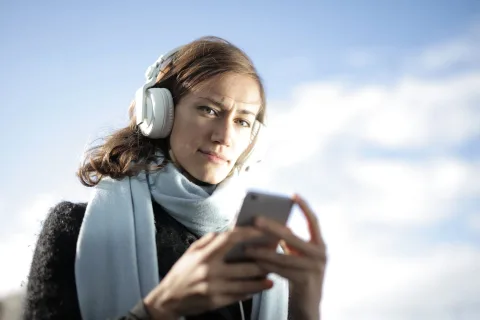 Une personne utilise son smartphone avec des écouteurs dans une rue calme pour pratiquer une langue étrangère.