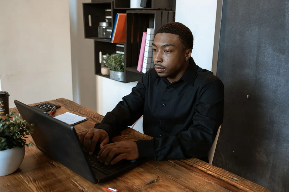 Un homme concentré travaillant sur son ordinateur portable dans un bureau épuré baigné de lumière naturelle.