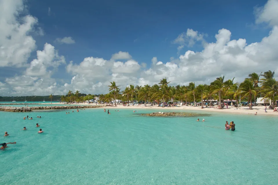 Plage de sable fin et eau turquoise transparente à Curaçao avec des parasols en paille