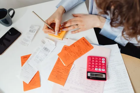 Une femme examine des devis de mutuelle santé avec une calculatrice sur une table de cuisine.