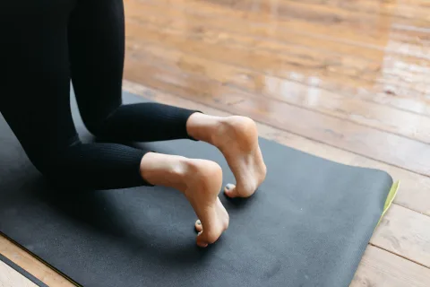 Femme pieds nus en équilibre sur une jambe sur un sol en bois clair à domicile.