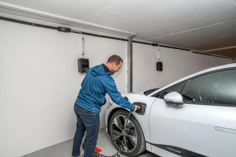 Une voiture électrique en train de charger sur une borne murale dans un parking souterrain d'immeuble.