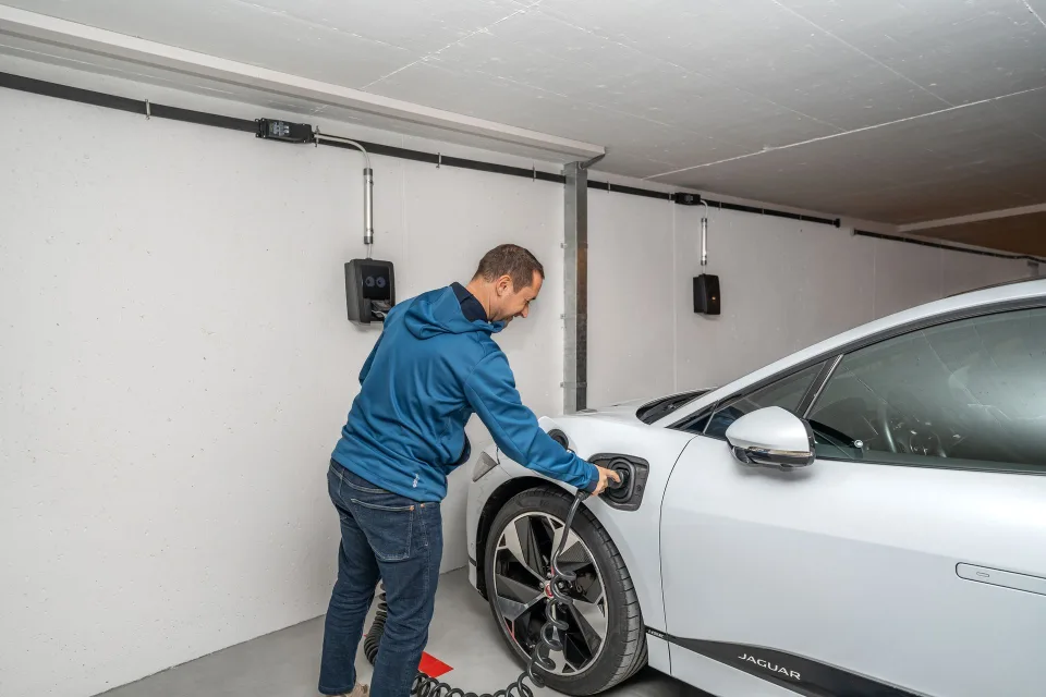 Une voiture électrique en train de charger sur une borne murale dans un parking souterrain d'immeuble.