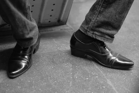 Gros plan sur une paire de jazz shoes en cuir noir portées avec un jean retroussé sur un trottoir en ville.