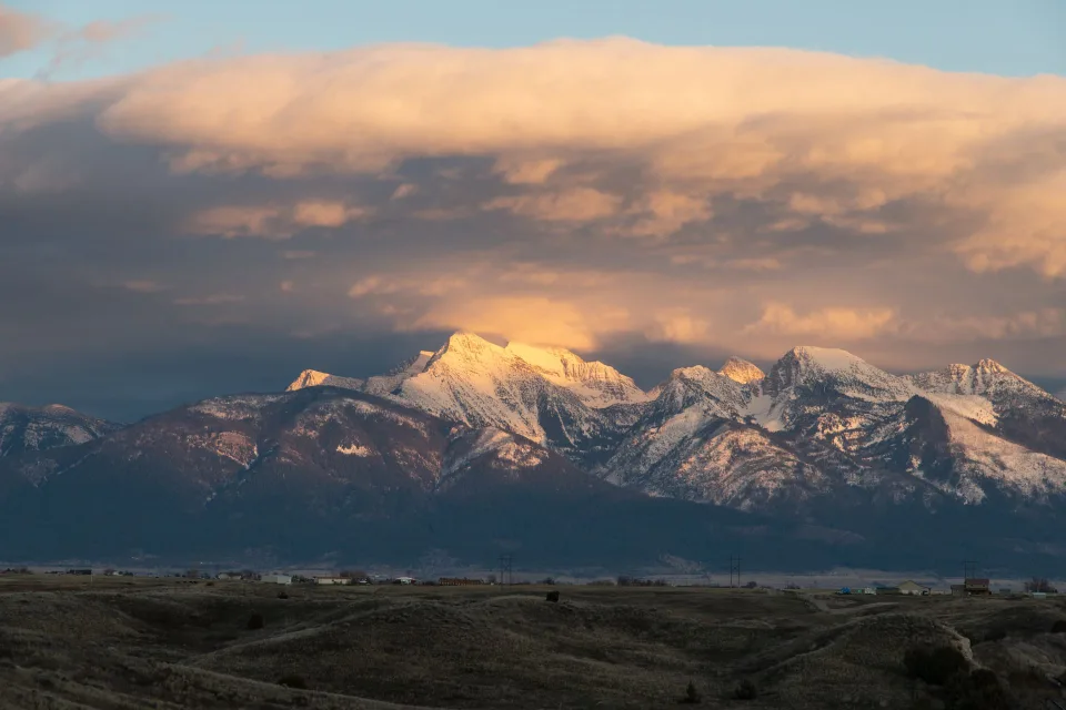 Un ranch en bois typique du Montana devant des montagnes rocheuses sous un ciel de coucher de soleil.