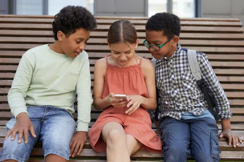 Un groupe d'amis assis en terrasse regardant ensemble l'écran d'un smartphone pour partager les frais de leur voyage.