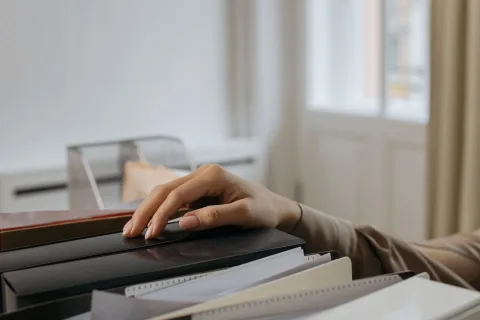 Des classeurs de différentes couleurs alignés sur une étagère de bureau en bois.