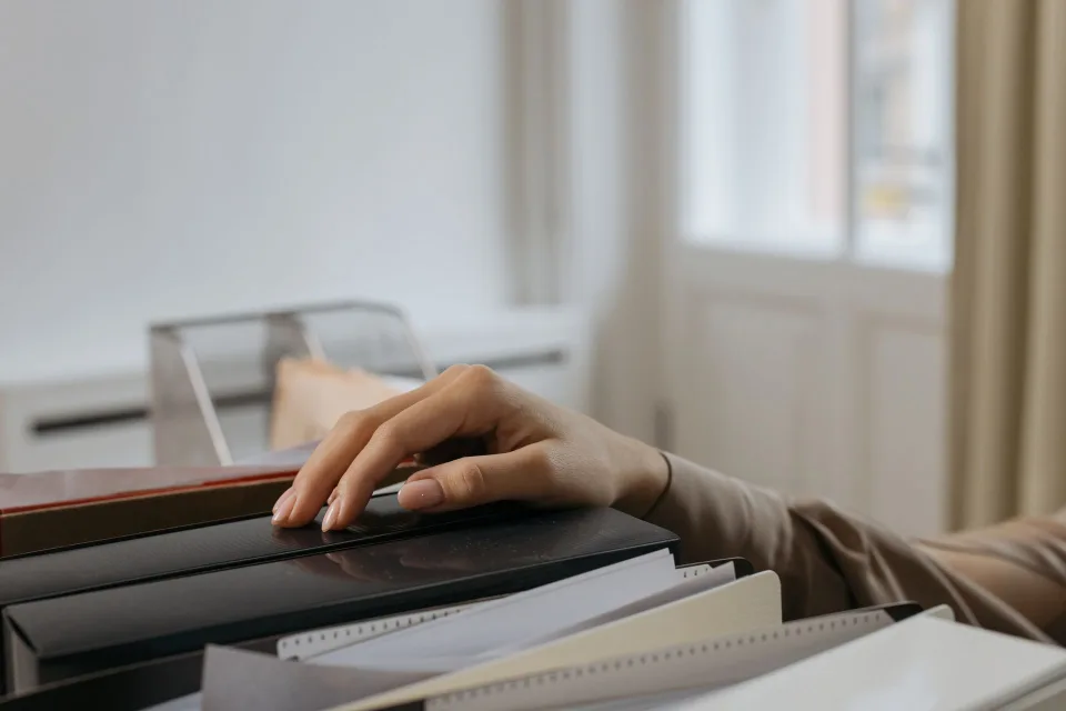 Des classeurs de différentes couleurs alignés sur une étagère de bureau en bois.
