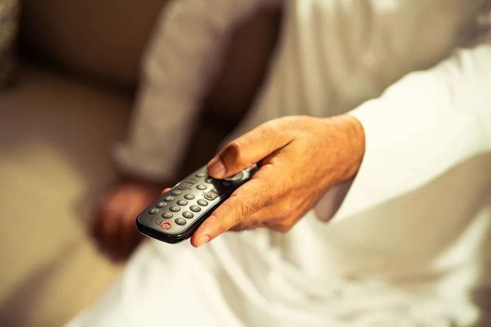 Une personne utilise une télécommande pour modifier les paramètres de l'image sur un grand écran de télévision dans un salon sombre.