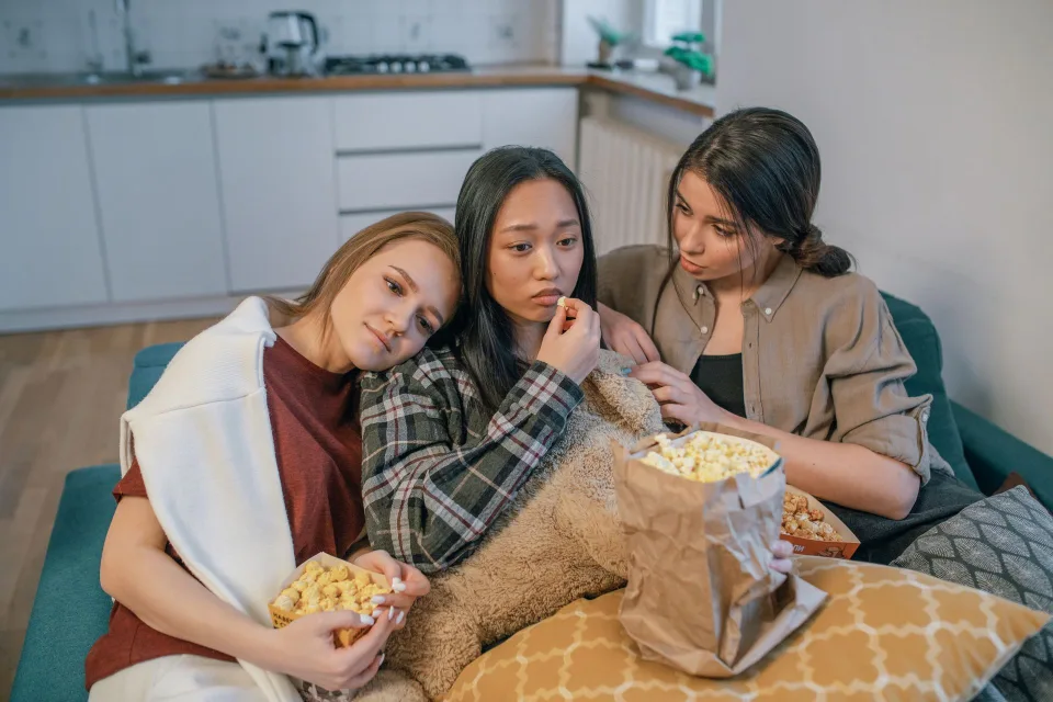 Groupe d'amis assis sur un canapé qui rient devant un écran de télévision.