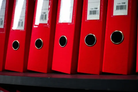 Des classeurs colorés bien rangés sur une étagère de bureau.
