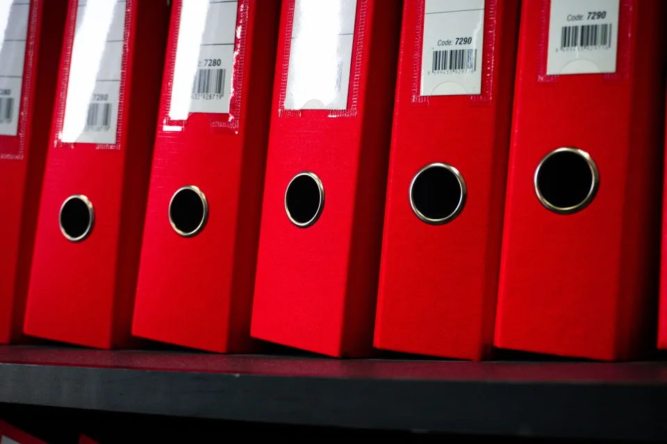 Des classeurs colorés bien rangés sur une étagère de bureau.